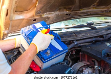 Maintenance Of The Machine. A Male Car Mechanic Takes Out A Battery From Under The Hood Of A Auto To Repair, Charge Or Replace It.