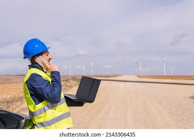 Maintenance Operator At A Wind Farm Talking To His Work Team On His Mobile Phone. Young Adult Man In Engineering Internship In Renewable Energy Installations.