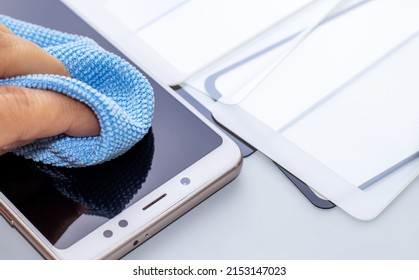 maintenance and repairing smartphones. hand is cleaning phone screen with blue napkin. many tempered glass screen protector.  mobile screen replacement protector. installation of protective cover film - Shutterstock ID 2153147023
