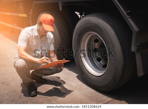 Maintenance\
and Vehicle inspection. A truck mechanic driver holding clipboard\
his checking safety a truck wheels and\
tires.