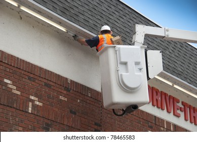 Maintenance worker in a bucket replacing fluorescent tubes on a commercial building