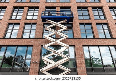 maintenance workers are repairing a modern building facade from an elevating scissor lift aerial work platform