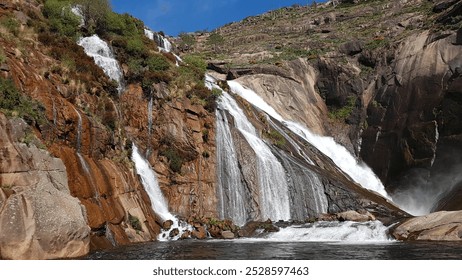 Majestic cascade, Rugged cliff, Misty spray, Sunlit water, Jagged rocks, Natural beauty, Spanish cliffs, Flowing water, Rocky terrain, Scenic view, Cascading falls, Cliffside waterfall, Serene nature. - Powered by Shutterstock