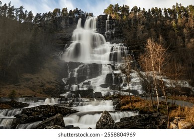 Majestic cascading waterfall flowing over rocky cliffs, surrounded by lush forest and bathed in soft light. - Powered by Shutterstock