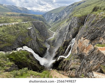 Majestic cascading waterfall flowing through a deep canyon surrounded by rugged cliffs and lush greenery in a picturesque mountain setting. - Powered by Shutterstock