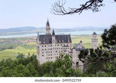 A majestic castle perched on a hill, surrounded by lush greenery and scenic landscapes, with distant mountains and a tranquil lake visible in the background. - Powered by Shutterstock