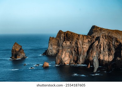 Majestic coastal cliffs with rugged rock formations rising from the deep blue ocean under clear sky .  - Powered by Shutterstock