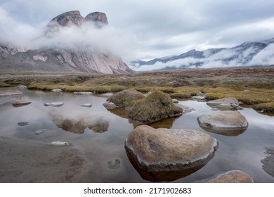 Majestic granite rocks reflect in water surface. Wild arctic landscape of Akshayuk Pass, Baffin Island, Canada on a cloudy, rainy day of arctic summer. Wild north.