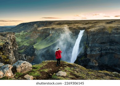 Majestic Haifoss waterfall flowing in volcanic canyon and traveler taking a picture among the Icelandic Highlands in summer at Iceland