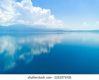 Majestic huge white thick clouds float across the clear blue daytime sky above the horizon with the shallow azure calm Adriatic Sea in the light of the bright summer sun