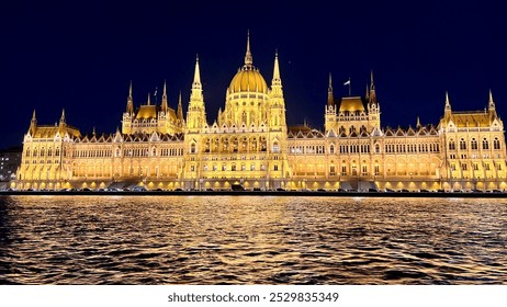 the majestic Hungarian Parliament Building in Budapest, Hungary, illuminated at night. The reflection of the lights on the Danube River adds a stunning effect under the clear night sky. - Powered by Shutterstock