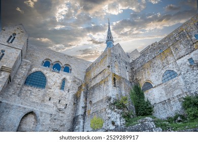 Majestic Mont Saint Michel Abbey rises against a dramatic sky, showcasing its Gothic architecture, stone walls, and iconic spire. A stunning view of this historic French landmark. - Powered by Shutterstock