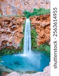 The majestic Mooney Falls cascades into a vibrant turquoise pool, surrounded by lush greenery and dramatic red canyon walls. This iconic desert waterfall is a breathtaking natural wonder.