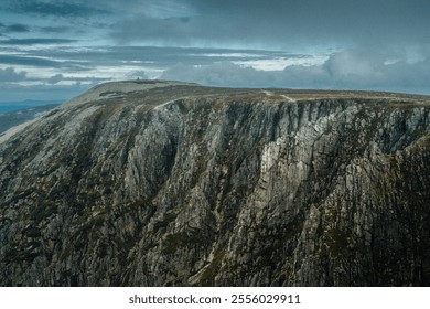 A majestic mountain, lush and verdant with trees, stands tall against a dramatic cloudy sky that looms in the background - Powered by Shutterstock