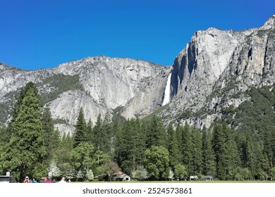 Majestic mountains from Yosemite Village, framed by a lush forest. A cascading waterfall adds to the beauty of the scene, showcasing the breathtaking natural landscape of the park. - Powered by Shutterstock