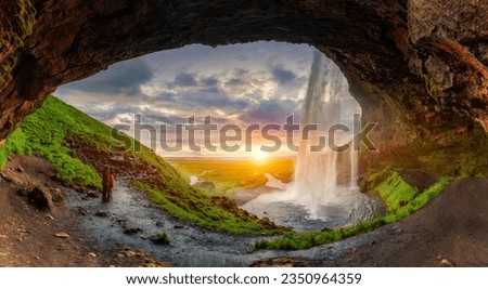 Majestic natural cave with sunset over Seljalandsfoss waterfall flowing and tourist enjoying in summer at South of Iceland