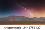 Majestic night sky with the Milky Way over orange desert sand, mountains and isolated palm trees. Copy space background or wallpaper.