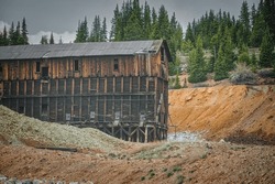 Majestic Old Mining Building Paired With Pine Trees And A Rugged Excavation Site In Colorado, Showcasing The Raw Nature And Mountainous Terrain Of The Heart Land