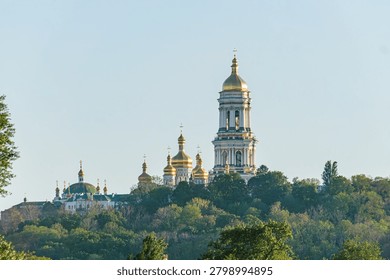 majestic religious complex featuring multiple golden domes, tall bell tower, stone and brick construction, dense greenery backdrop, clear bright sky day, conveying spirituality, history, cultural he.
