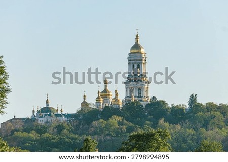 majestic religious complex featuring multiple golden domes, tall bell tower, stone and brick construction, dense greenery backdrop, clear bright sky day, conveying spirituality, history, cultural he.