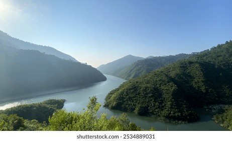 Majestic River Valley Amidst Verdant Mountains. A serene river winds gracefully through lush, forested mountains under a clear blue sky, capturing nature's tranquil beauty in the golden morning light - Powered by Shutterstock