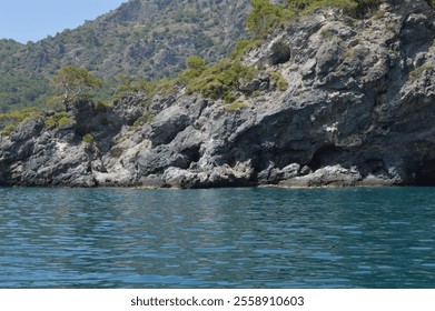 Majestic rocky cliffs meeting the tranquil turquoise waters of Oludeniz, Turkey, surrounded by lush green hills under a clear blue sky - Powered by Shutterstock