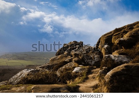 Majestic rocky landscape with sunlit grass under a blue sky with clouds at Brimham Rocks, in North Yorkshire