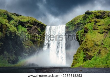 Majestic Skogafoss waterfall flowing with rainbow and moody sky in summer at Iceland. Icelandic famous place, Landscape popular attraction