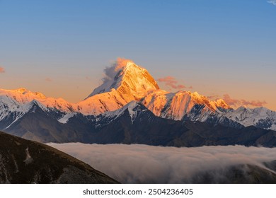 A majestic snow-capped mountain glows warmly at sunrise, towering over soft, drifting clouds below, with a serene blue and pink sky providing a tranquil backdrop. - Powered by Shutterstock