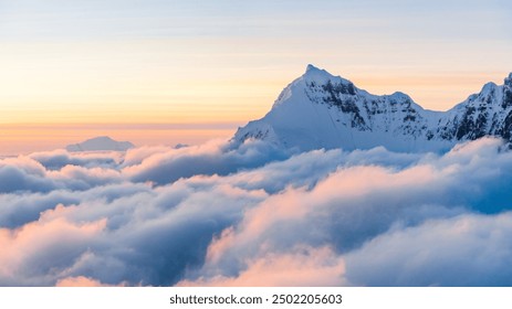 A majestic snow-capped mountain peaks rise above a sea of clouds at sunrise, bathed in warm golden light - Powered by Shutterstock