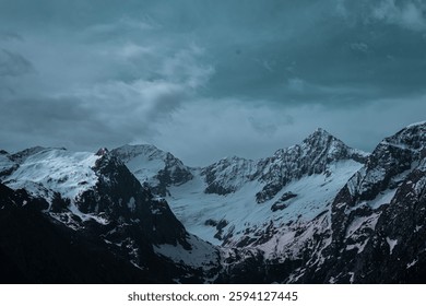 Majestuosos picos montañosos cubiertos de nieve se elevan bajo un dramático cielo verde azulado, evocando aventura, soledad y asombro. Ideal para viajes, naturaleza o diseños de temática invernal que buscan una belleza robusta. Un telón de fondo atemporal