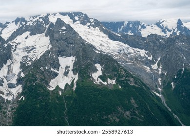 Majestic Snow-Capped Mountains With Rocky Peaks Under Cloudy Sky in Summer - Powered by Shutterstock