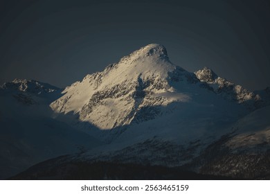 Majestic snow-covered mountain peak illuminated by soft sunlight against a dark sky, showcasing natural beauty and tranquility. - Powered by Shutterstock