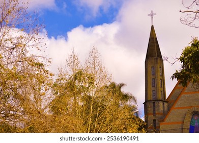 A majestic stone church tower reaches toward the sky, showcasing intricate architectural details. The blurred background enhances the tower's prominence against a clear blue sky. - Powered by Shutterstock