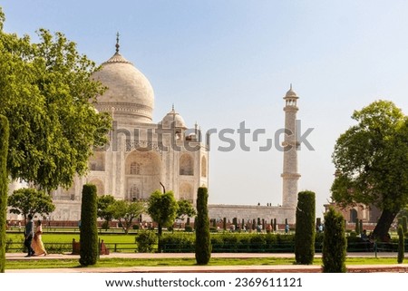 A majestic Tajmahal, one of the world's seven wonders is viewed along with its minaret and lush green garden. A clear blue sky adds magnificence to the white marble of the beautiful structure.
