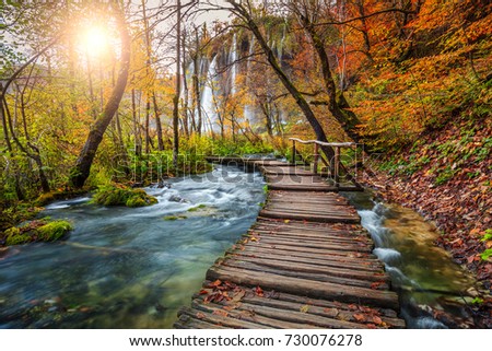 Majestic touristic wooden pathway in the colorful autumn deep forest with clean brook and spectacular waterfalls, Plitvice National Park, Croatia, Europe