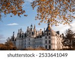 A majestic view of Chateau de Chambord framed by autumn leaves under a clear sky on a sunny day in France