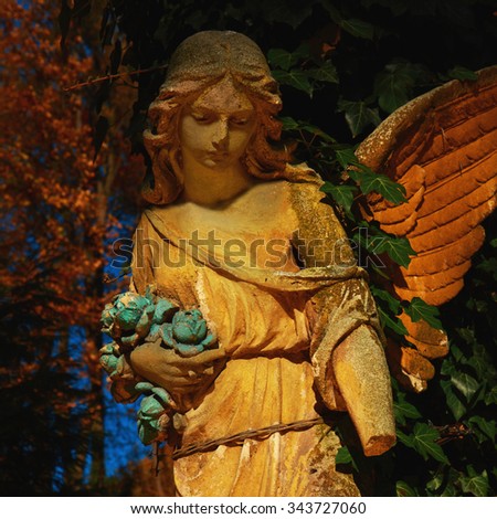 Majestic view of statue of golden angel illuminated by sunlight against a background of dark foliage. Dramatic unusual scene. Beauty statue.
