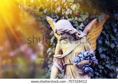 Majestic view of statue of golden angel illuminated by sunlight against a background of dark foliage. Dramatic unusual scene. Beauty statue. 
