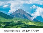 A majestic volcano in El Salvador rises above lush green hills, surrounded by clouds and a vibrant blue sky, showcasing the natural beauty and power of this dramatic landscape.