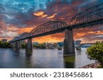 the majestic Walnut Street Bridge over the rippling blue waters of the Tennessee River surrounded by lush green trees and buildings with powerful clouds at sunset at Coolidge park in Chattanooga	