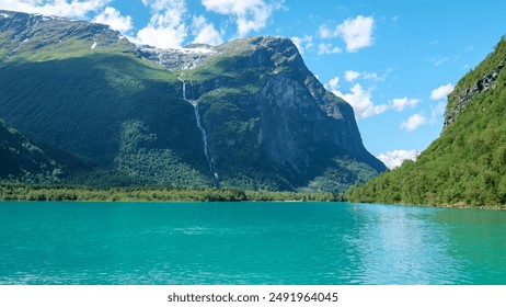 A majestic waterfall cascades down a green mountainside, mirroring the vibrant blue of a tranquil lake. Lush foliage and snow-capped peaks complete the breathtaking scenery. Lovatnet lake Lodal valley - Powered by Shutterstock