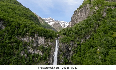 Majestic Waterfall Cascading Down Rocky Cliff Surrounded by Lush Green Forests and Snow-Capped Mountains at Sunrise - Powered by Shutterstock