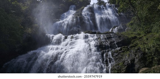 Majestic waterfall cascading down rocky cliffs, surrounded by lush green foliage. Mist rises, creating a serene and powerful natural scene. - Powered by Shutterstock