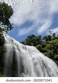 Majestic Waterfall Under Dramatic Cloudy Blue Sky in Tropical Rainforest