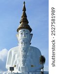 A majestic white Buddha statue with five faces stacked in ascending order, topped by an ornate golden spire. The sky in the background adds to the serene and spiritual atmosphere.