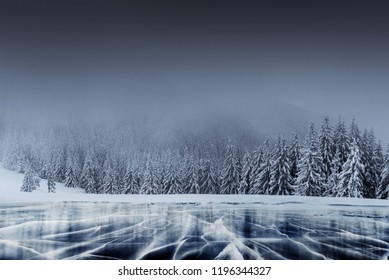 Majestic winter landscape with cracks on the surface of the blue ice. Frozen lake in winter mountains. A dramatic scene with low black clouds, a calm before the storm.