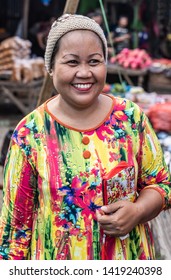 Makassar, Sulawesi, Indonesia - February 28, 2019: Terong Street Market. Portrait of smiling woman with colorful dress and hat. Background is faded market booths.