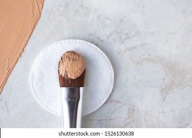 Make up brush with BB cream, CC cream or foundation on white cotton round and luxury marble background, top view. Daily makeup