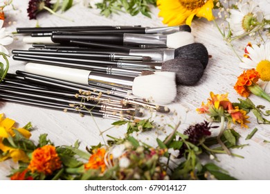 Make up brushes on a table next to wild flowers on wooden background
